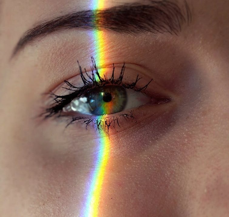 Closeup of crop anonymous sad female with green eyes and rainbow light on face looking at camera
