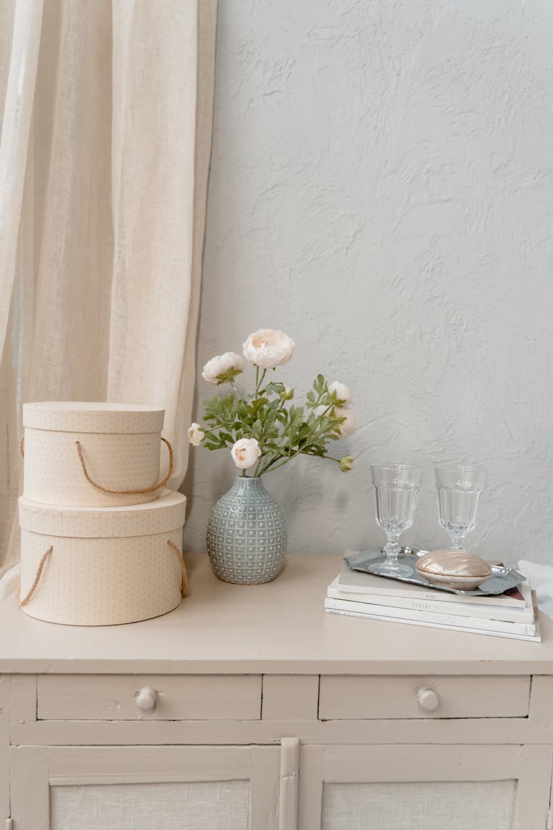 A minimalist still life featuring flowers in a vase, decorative boxes, and glassware.