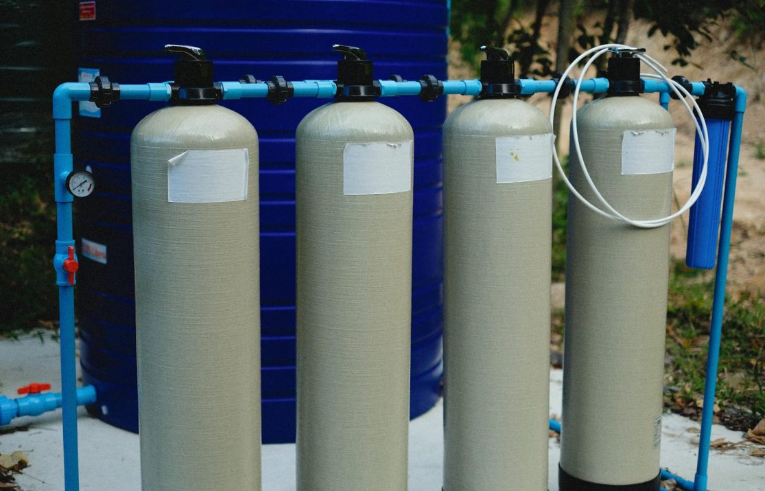 Four beige tanks in an outdoor water treatment setup with blue piping.