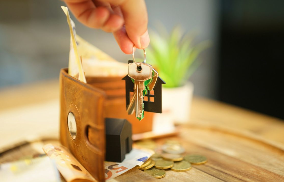 Hand holding keys with house charm and wallet.