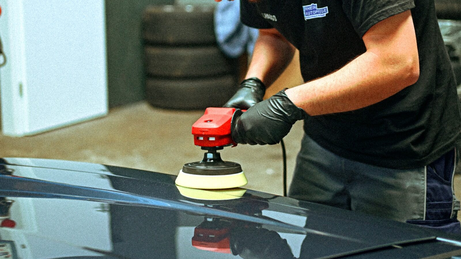 A person polishes a dark car with an electric polisher.